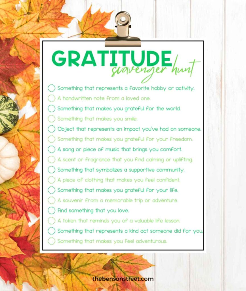 A gratitude scavenger hunt list on a clipboard with autumn leaves. The list includes prompts like “Find something that makes you smile” and “A souvenir from a memorable trip.”.
