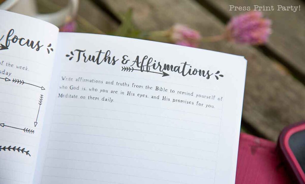 An open prayer journal for women displays a page titled "Truths & Affirmations," featuring text that encourages writing affirmations from the Bible. In the background, blurred flowers and a wooden table create a serene setting for reflection and spiritual growth.