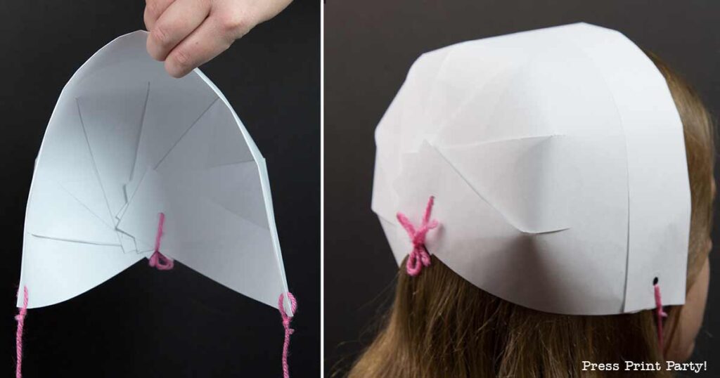 Person wearing a white paper pilgrim bonnet secured with pink yarn. The image showcases a side view of the bonnet on the head, along with a close-up of the internal paper folds, highlighting this charming DIY project.