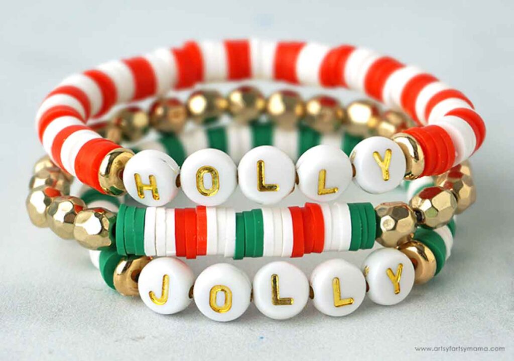 Three festive bracelets perfect for Christmas crafts for teens, featuring beads in red, green, white, and gold. The top bracelet spells "HOLLY" while the bottom one spells "JOLLY," both adorned with gold letters on white beads.