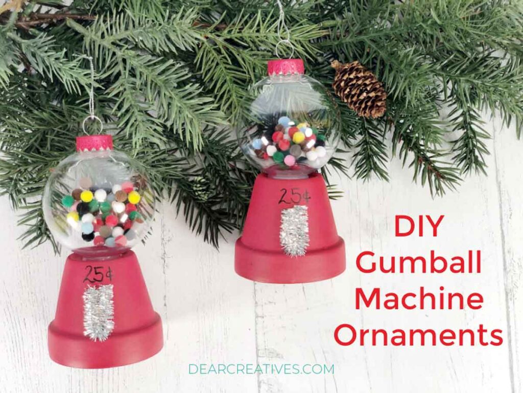 Two DIY gumball machine ornaments hang on a pine branch, ideal for Christmas crafts for teens. Each ornament has a clear globe filled with colorful beads and a red base marked "25¢", with silver pipe cleaner details. The background is a white wooden surface. Text reads "DIY Gumball Machine Ornaments".