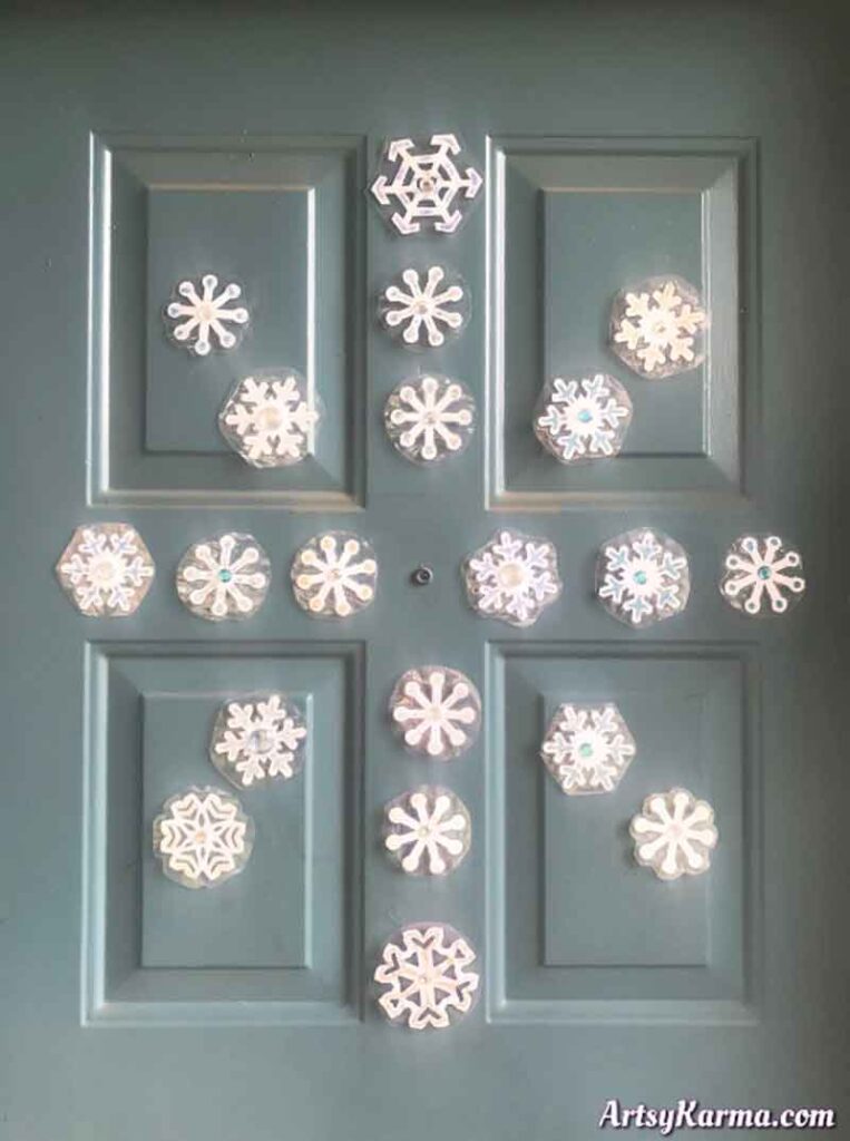 The closed door, a charming showcase of Christmas crafts for teens, features various white paper snowflakes intricately arranged in a cross pattern against a soft teal background.