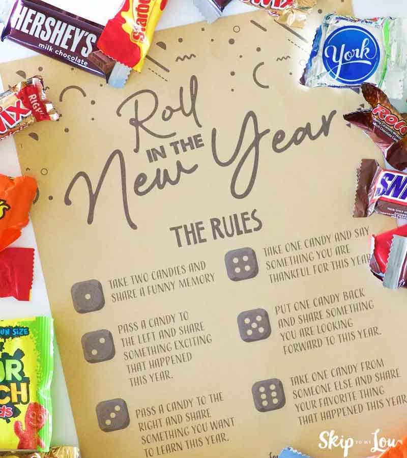 A New Year-themed board game with dice rules is surrounded by chocolate and candy, including Hershey's, York, and Twix. The game involves taking candies and sharing reflections or gratitude about the past year.