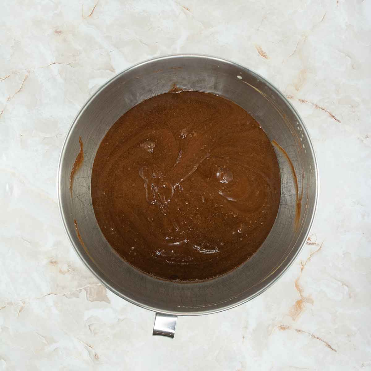 A mixing bowl holds the smooth, dark brown batter of a 4 ingredient flourless chocolate cake on a marble countertop.