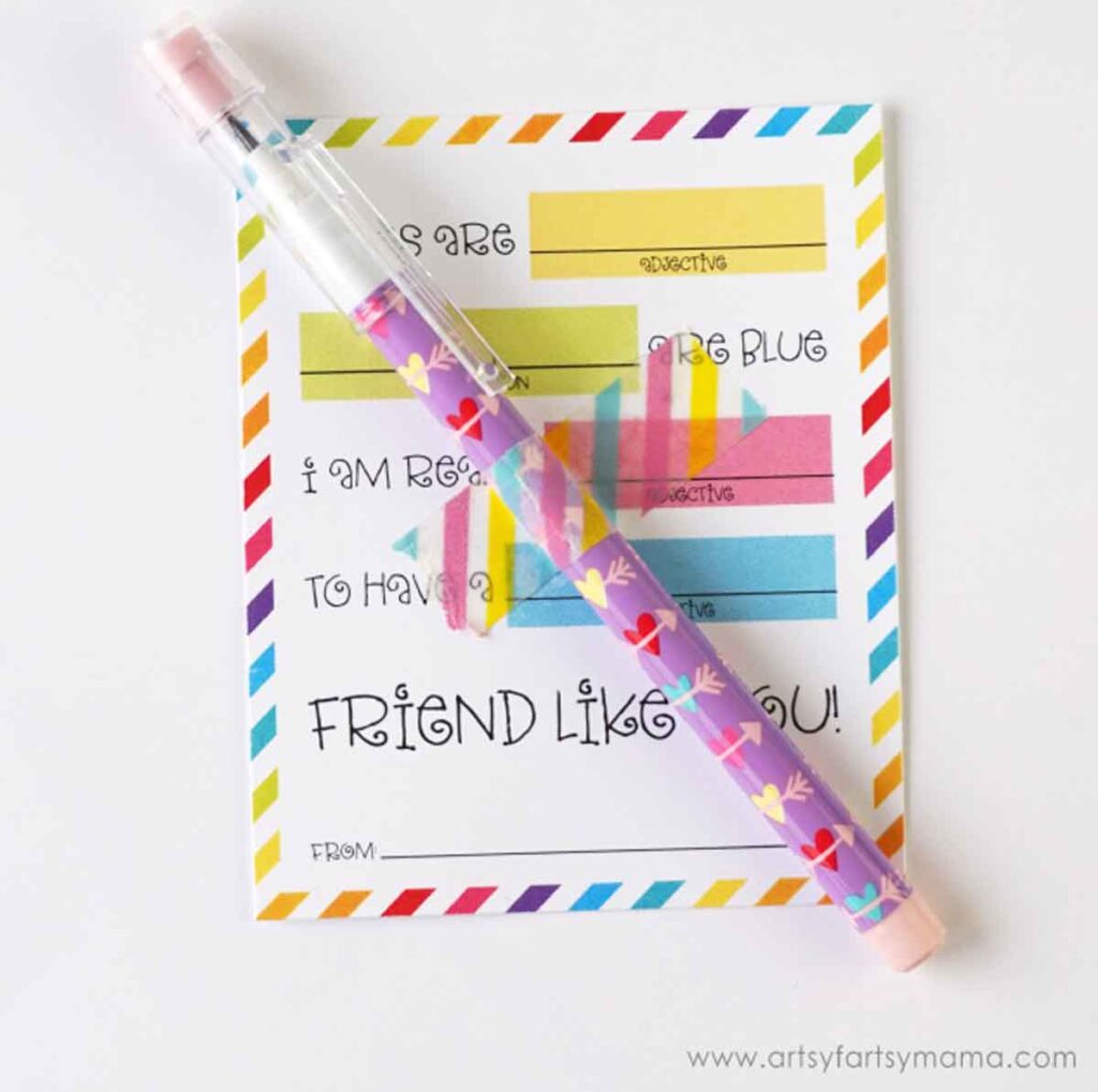 A colorful friendship card with fill-in-the-blank prompts on a striped background sits underneath a purple, heart-adorned pen. It's the perfect companion for writing out pencil valentines. The corner of the card reads "From" with a website watermark in the lower right corner.