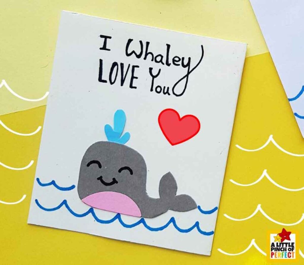 A handmade card with a smiling gray whale and red heart. Text reads, "I Whaley LOVE You." The background features yellow and white waves.