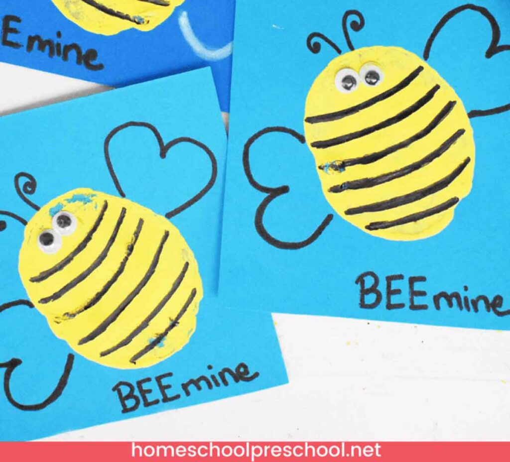 A handmade valentine card featuring a yellow and black striped bee on a blue background. The bee has googly eyes and heart-shaped wings. The text reads "BEE mine." This delightful paper craft is part of a children's project from homeschoolpreschool.net.