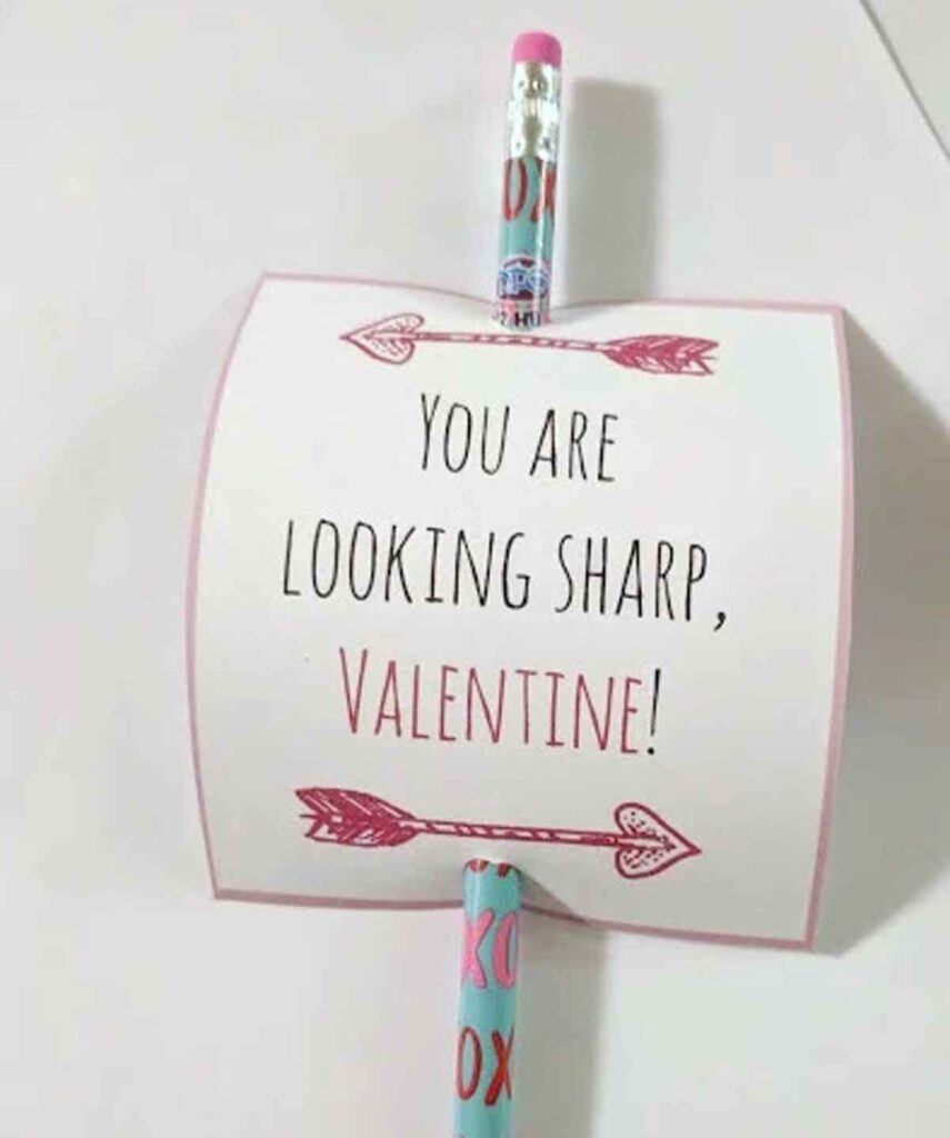 A pencil valentine inserted through a card with the message, "You are looking sharp, Valentine!" The card features pink and red arrows and heart designs, with the pencil also decorated with hearts and text.