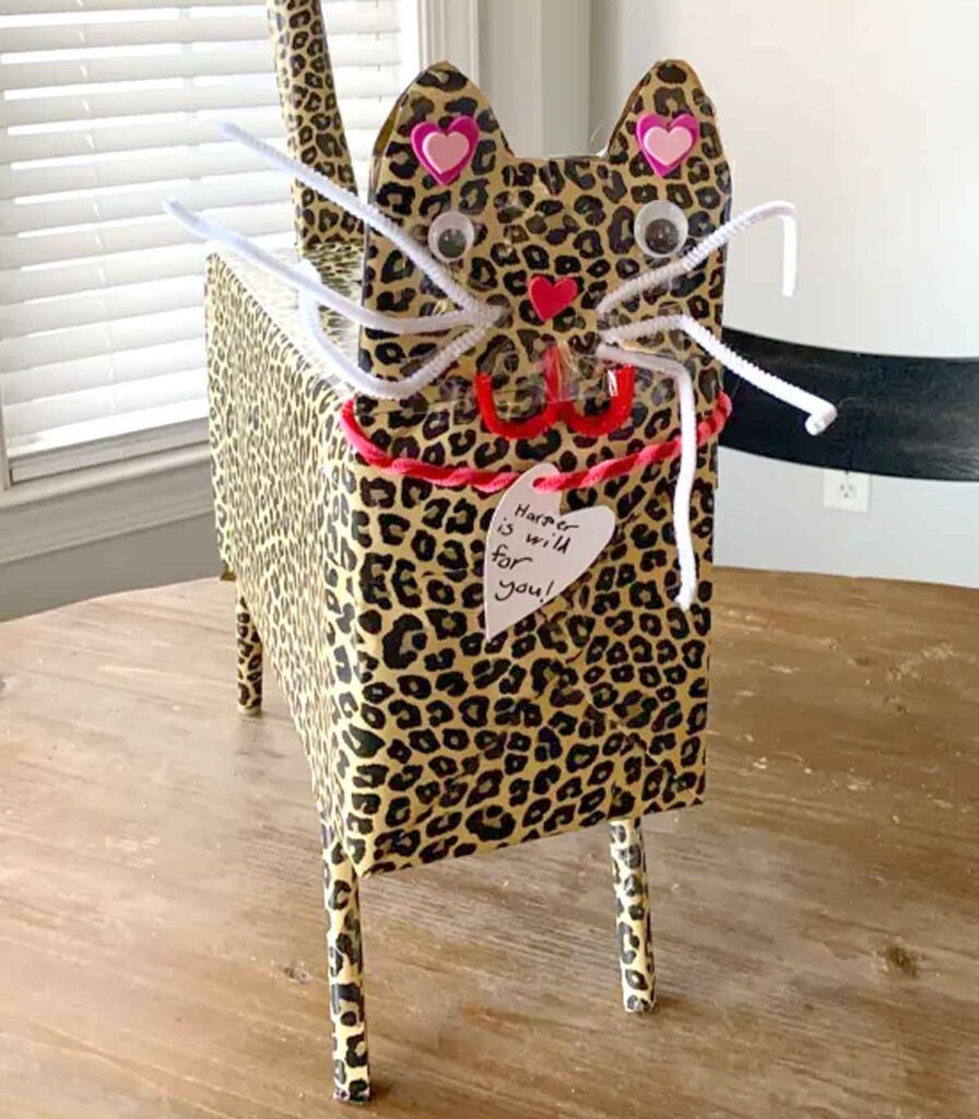 A perfect valentine box idea for school, this homemade cat-shaped creation boasts a chic leopard print. Adorned with googly eyes, a heart nose, and pipe cleaner whiskers, it has a paper note reading "Here is a fur you." Set charmingly on a wooden table, it's sure to delight classmates.