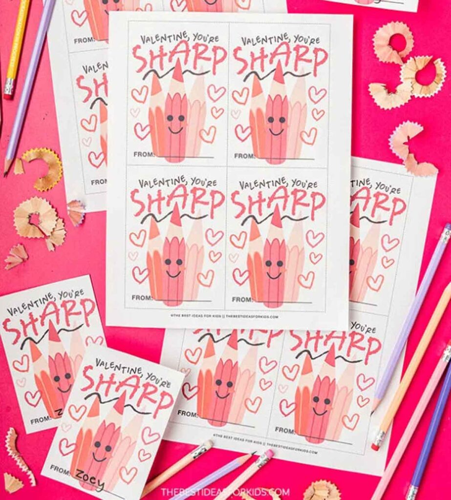 Cartoon pencil valentines featuring the message "Valentine, you're sharp!" are scattered on a pink background. Colored pencils and pencil shavings add a whimsical touch to the scene.