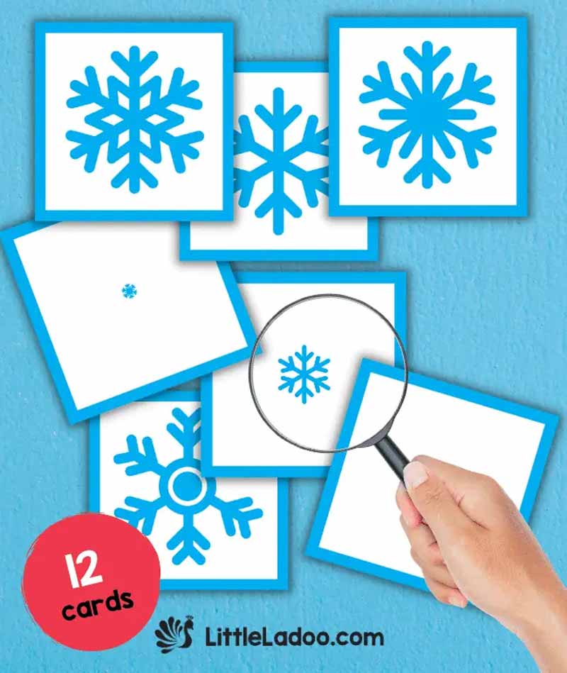 A hand holding a magnifying glass over seven cards, each featuring a different blue snowflake on a white background. Perfect for printable winter games, the text reads "12 cards" and "LittleLadoo.com" in the bottom corner.