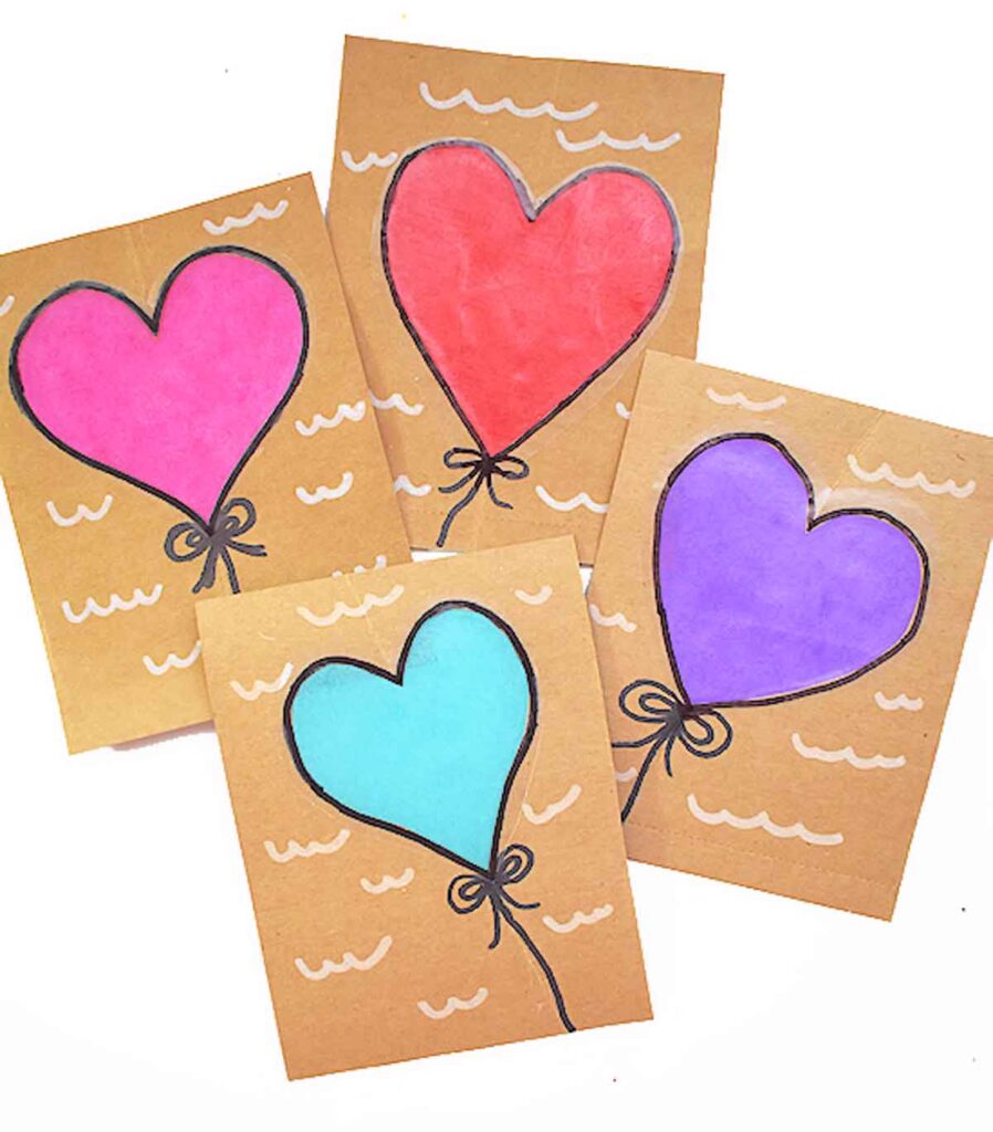 Four handmade Valentine paper crafts feature heart-shaped balloons on brown paper. Each heart balloon boasts a unique color: pink, red, blue, and purple. With black outlines and strings, the balloons are set against wavy lines that add a charming background decoration.