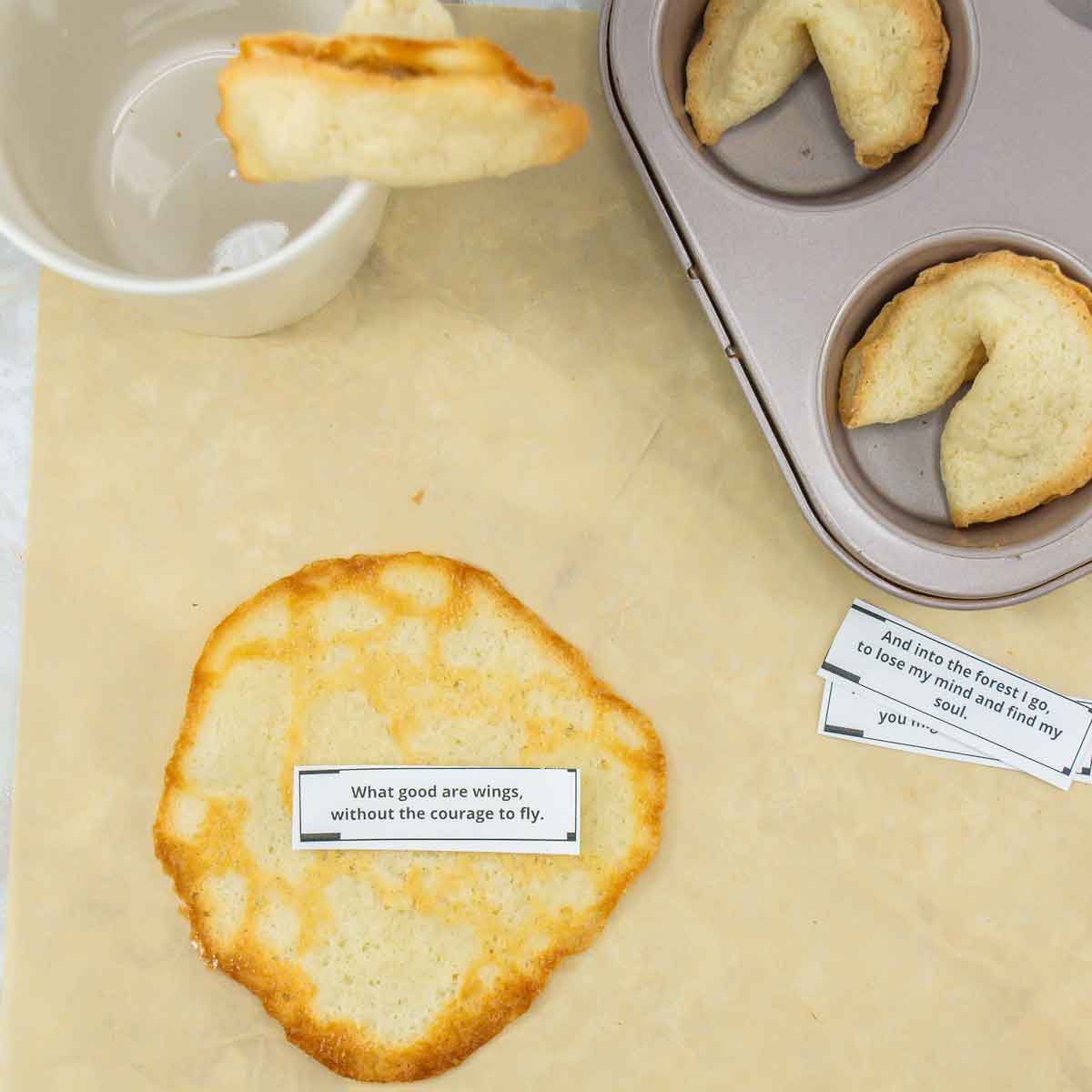 A fortune cookie is shown next to a baking tray with cookies, a cup, and a fortune slip saying, "What good are wings without the courage to fly?" Two other fortune slips are partially visible.