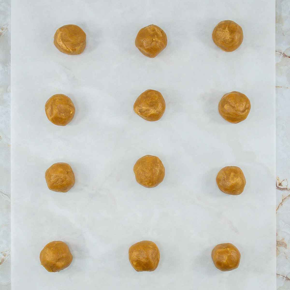 Twelve perfectly spaced 3 Ingredient Peanut Butter Cookies rest on a sheet of parchment paper, ready for baking.
