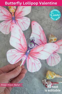 A hand holds a lollipop with pink butterfly wings. More butterfly-themed lollipops rest on a gray surface, alongside text promoting 