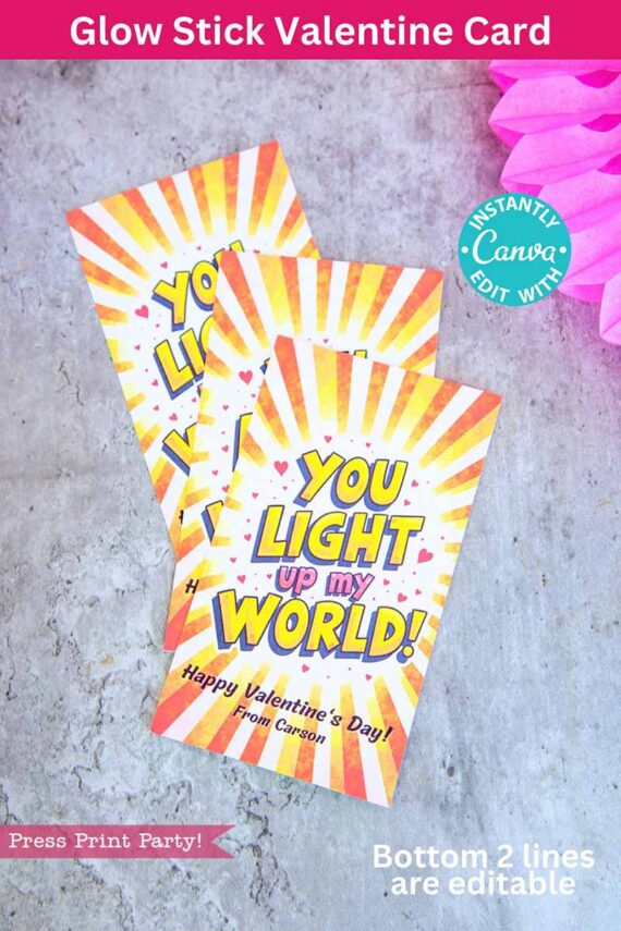 Two colorful Valentine's cards on a textured surface showcase a sunburst design. The text reads "You Light Up My World! Happy Valentine's Day!" with editable lines below. A pink tissue decoration is partially visible in the background. Product Name: template (Copy) (Copy).