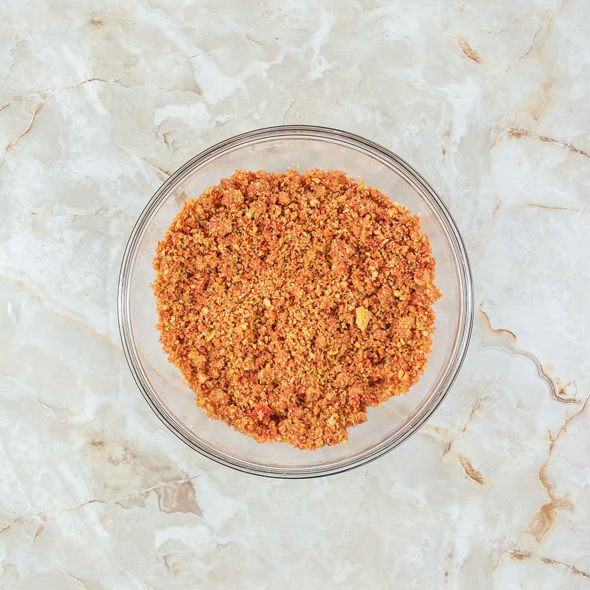 A clear glass bowl filled with a mixture of finely ground, orange-brown spices on a marbled, light beige surface.