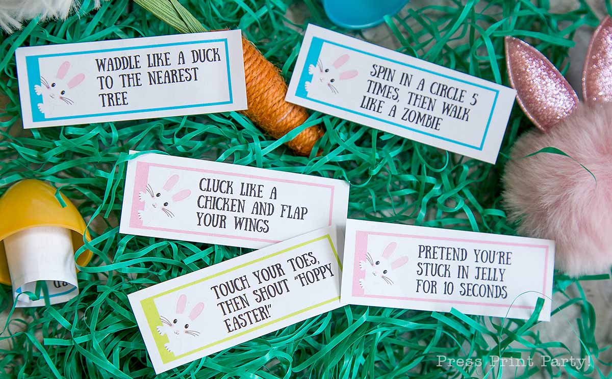 Colorful Easter-themed activity cards are set on green grass, perfect for an easter egg hunt. With playful actions like waddling like a duck or clucking like a chicken, they'll add fun to any gathering. Nearby, bunny ears and an egg shaker wait to join the festive antics.