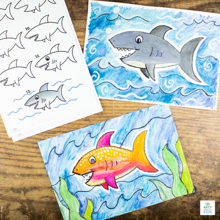Step-by-step shark drawing instructions and two colorful watercolor paintings of sharks are displayed on a wooden surface; one shark is gray, the other is orange and yellow, both swimming in blue ocean scenes.