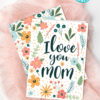 The Floral Mothers Day Card - Whimsy features "I love you MOM" with colorful flowers and leaves on pink fabric. Includes labels: "INSTANT PDF DOWNLOAD" and "Folds to 5” x 7”, Blank inside.