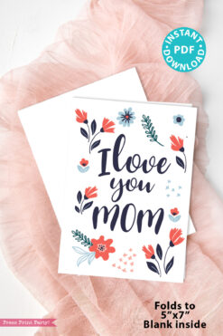 The Floral Mothers Day Card - Whimsy features elegant designs and "I love you MOM" on the front, resting on a white envelope atop pink fabric. A teal badge says "INSTANT DOWNLOAD PDF." Folds to 5"x7", blank inside.