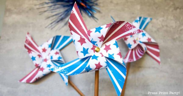 Three patriotic pinwheels with red, white, and blue star and stripe patterns on wooden sticks, arranged for a festive, patriotic celebration.