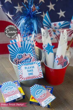 this patriotic party table includes an American flag backdrop, red and silver buckets with star-wrapped napkins, sparklers, and “Let Freedom Ring” and “Happy Independence Day!” printables.