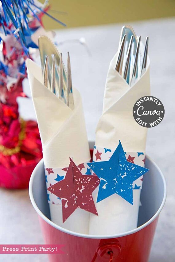 Two sets of silverware wrapped in white napkins with patriotic star decorations are arranged in a red bucket, with a vibrant table centerpiece in the background. Product shown: template