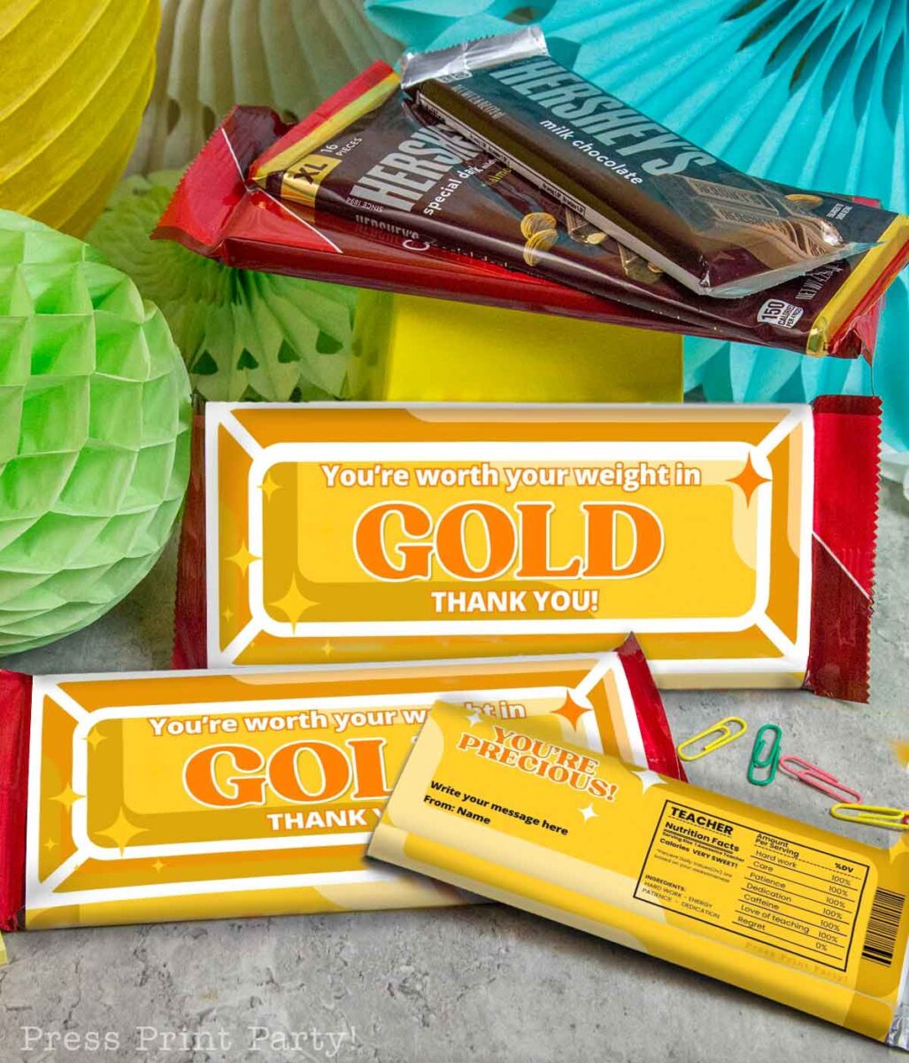 Several chocolate bars are wrapped in gold-themed "You're worth your weight in gold, thank you!" wrappers—perfect as a volunteer appreciation gift—surrounded by colorful paper decorations, paper clips, and a yellow box.