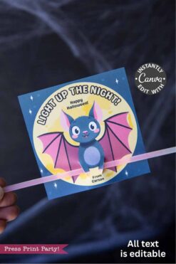 A hand holds the Cute Ghost Halloween Gift Card Holder, a Canva-editable card designed to hold a glow stick. It features a cute cartoon bat with pink wings and the phrase โLight Up the Night! Happy Halloween! From Carson.โ.