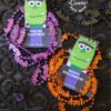 The Cute Ghost Halloween Gift Card Holder features a green Frankenstein cartoon and ghost accents with phrases like "You're Electric!" and "Happy Halloween!" and comes attached to purple and orange bat-shaped necklaces.
