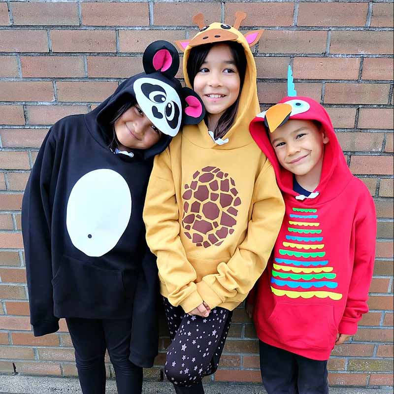 Three children stand smiling in front of a brick wall, each wearing a colorful animal-themed hoodie—a black and white panda, a yellow giraffe, and a red bird—perfect family costume ideas for playful group photos.