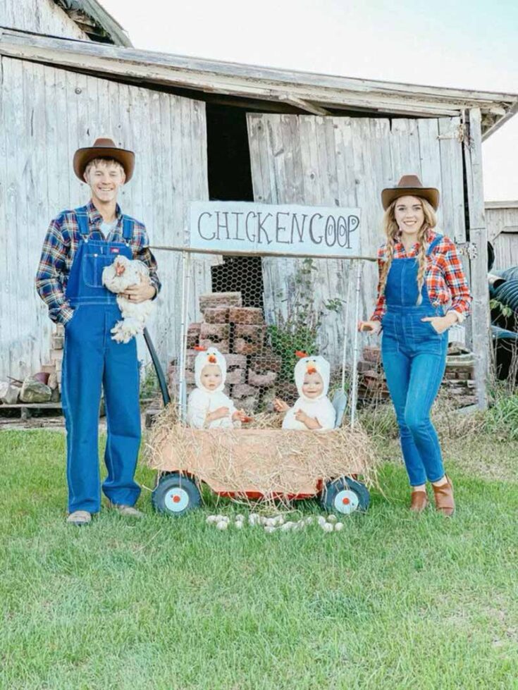A family in farm costumes stands by a rustic barn; two adults in overalls and cowboy hats flank a wagon with hay, a "CHICKEN COOP" sign, and two children dressed as chickens inside—charming inspiration for creative family costume ideas. A man holds a white chicken.