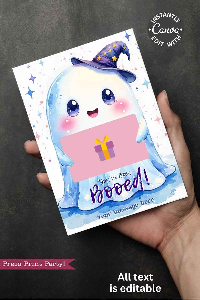 A hand holds the Cute Ghost Halloween Gift Card Holder, featuring a smiling ghost in a wizard hat, colorful stars, "You've been Booed!" text, space for a custom message, and a pink gift icon partially covering the card.