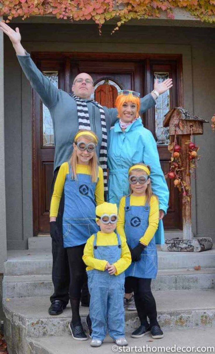 A family of five in costumes poses on a porch; two adults are dressed as Gru and Lucy, and three children are dressed as Minions from "Despicable Me." Autumn leaves decorate the area—perfect inspiration for family costume ideas.