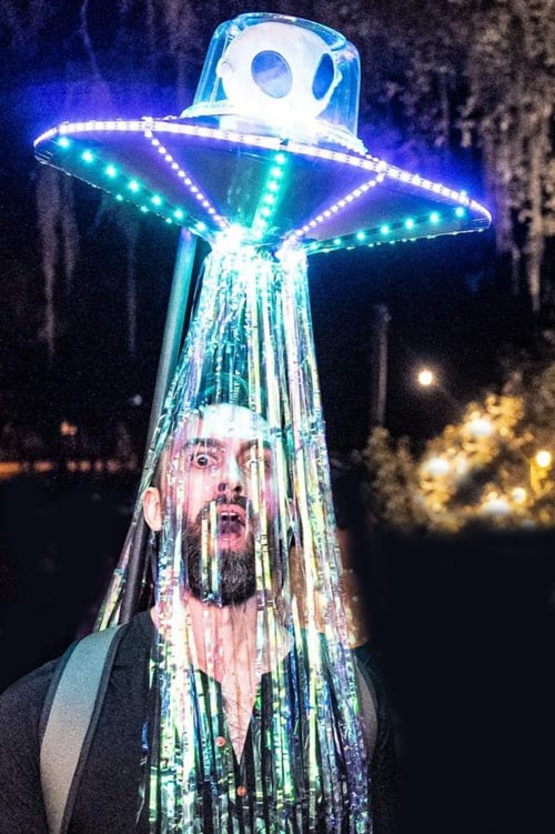 A person wears a glowing UFO costume with lights and shiny streamers hanging down, creating the illusion of being abducted by an alien spaceship at night.