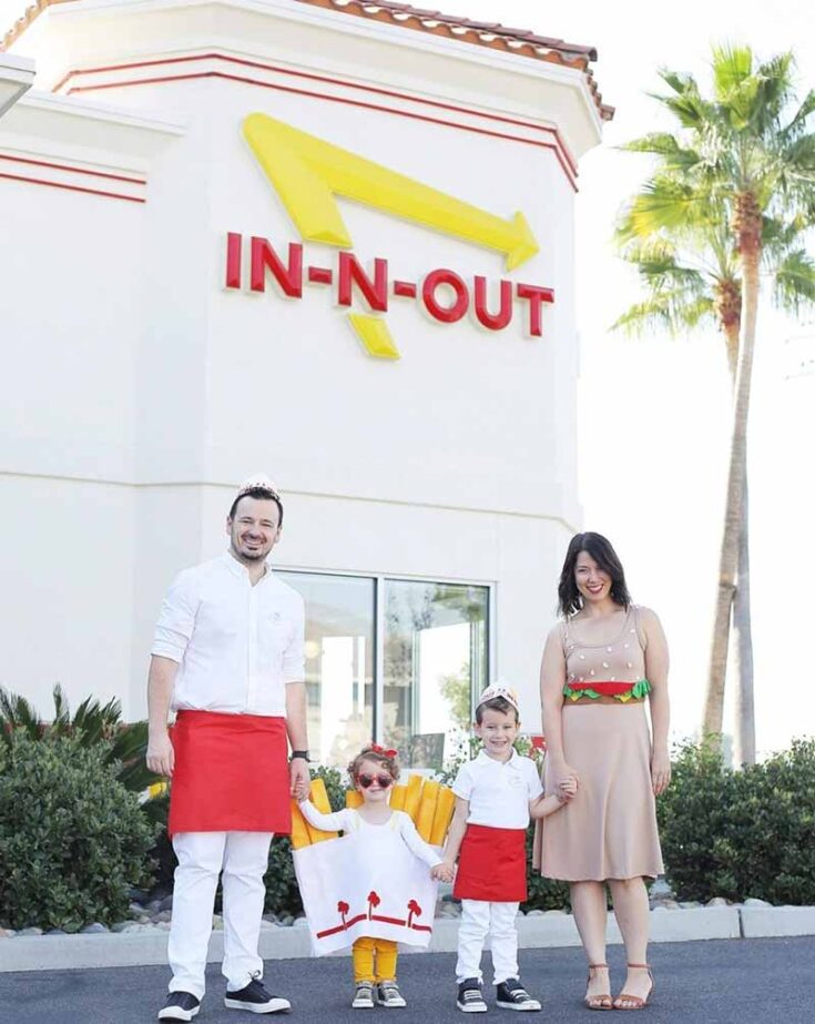 A family of four showcases creative family costume ideas outside an In-N-Out Burger. The father and one child wear In-N-Out uniforms, another child is dressed as fries, and the mother rocks a burger outfit, with palm trees swaying behind them.