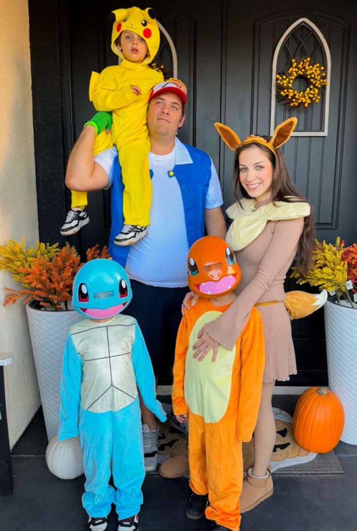 A family dressed in Pokémon costumes stands by a front door with fall decorations—perfect for those seeking fun family costume ideas. Dad is Ash holding a Pikachu-clad child; mom is Eevee, and two kids are Squirtle and Charmander.
