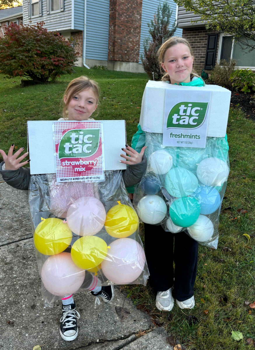 Two children smile at the camera in creative tic tac costume designs—one as strawberry mix with pink and yellow balloons, the other as freshmints with blue and white balloons, both perfectly capturing the fun of Tic Tac containers.