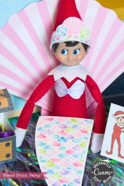 An Elf on the Shelf doll sports a festive red outfit and is surrounded by decorations and props from the Elf on the Shelf Movie Night Printable Kit, creating a magical holiday movie night scene.