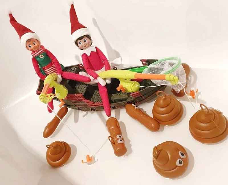 Two toy elves sit in a small toy boat, fishing with nets and rods for floating plastic poop and brown objects—a hilarious elf on the shelf poop idea sure to make everyone laugh.