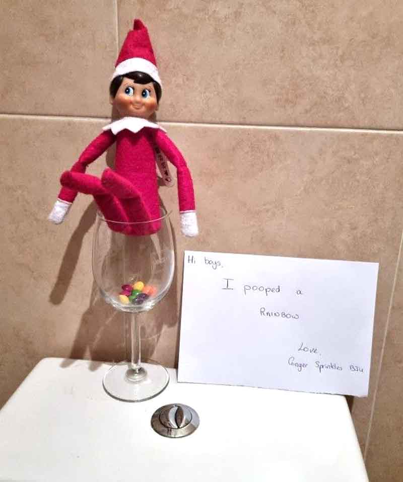 An Elf on the Shelf doll sits on a wine glass filled with colorful candies, resembling poop. Next to it is a note: "Hi boys, I pooped a rainbow. Love, Ginger Sparkles Blu." Try this for fun elf on the shelf poop ideas!.