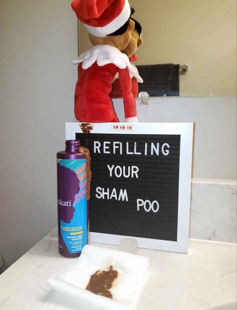 A plush elf doll sits on a bathroom counter beside a sign that says "REFILLING YOUR SHAM POO." This hilarious scene is perfect for those searching for quirky elf on the shelf poop ideas, with spilled shampoo resembling poop for extra laughs.