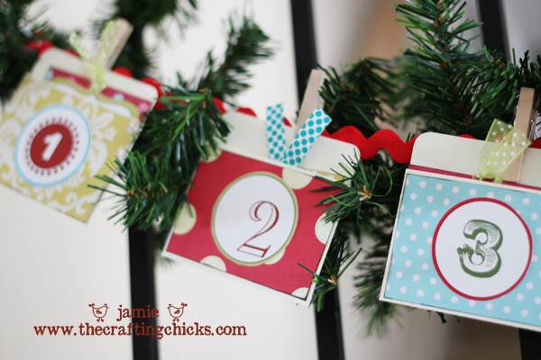 Three numbered cards (1, 2, and 3) with colorful patterns are clipped to green garland with ribbon. The image includes the website www.thecraftingchicks.com in red text.