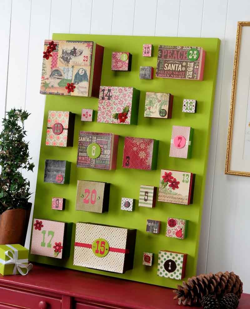 A green board displays 24 colorful, decorated boxes arranged in a grid, each numbered for an Advent calendar. The boxes have various festive patterns and sit on a red table next to a small potted plant. advent calendar ideas for adults