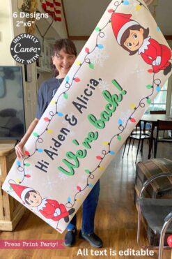 A woman smiles holding the Elf on the Shelf Arrival Banners, Girl and Boy, featuring “Hi Aiden & Alicia! We’re back!” with elves, snowflakes, and string lights—ideal for an indoor Elf on the Shelf movie night.