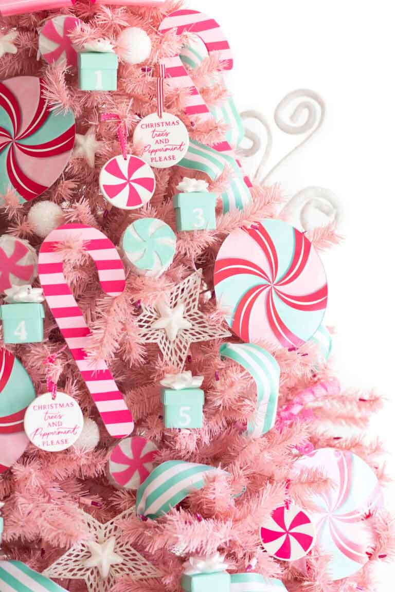 A pink Christmas tree decorated with large pastel candy-themed ornaments, including peppermint swirls, candy canes, stars, gift boxes, and round tags that say "Christmas and candy canes, please.