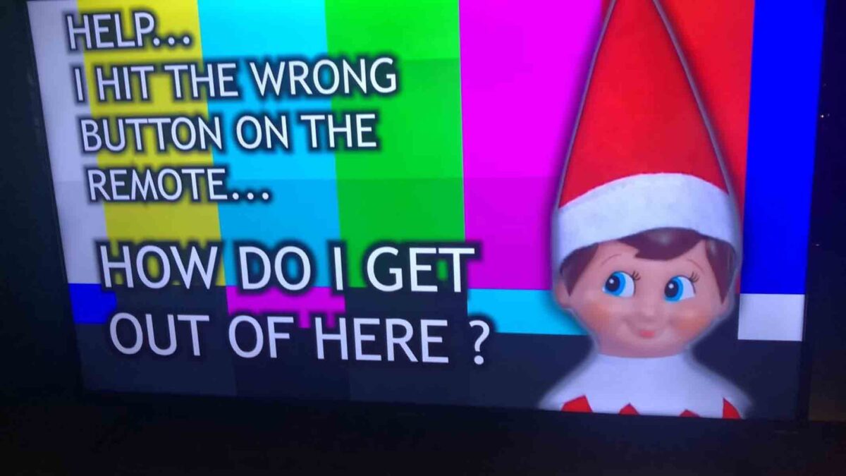 An elf doll appears beside a colorful TV test pattern with text saying, "HELP... I HIT THE WRONG BUTTON ON THE REMOTE... HOW DO I GET OUT OF HERE?.