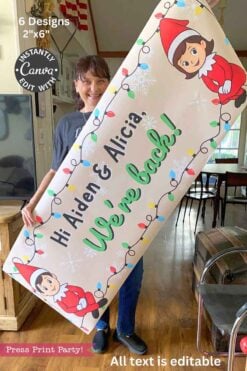A smiling woman holds the "Elf Arrival Banners Printable, Girl and Boy," featuring cartoon elves, holiday lights, and "Hi Aiden & Alicia! We're back!" in a cozy room with wooden furniture.