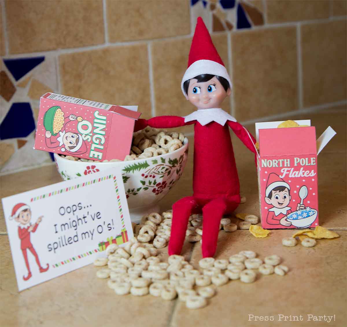 A toy Elf on the Shelf sits next to a bowl of spilled Cheerios, surrounded by miniature cereal boxes and a sign that reads, "Oops... I might've spilled my O's!"—all accented with fun printable elf on the shelf props on the kitchen counter.